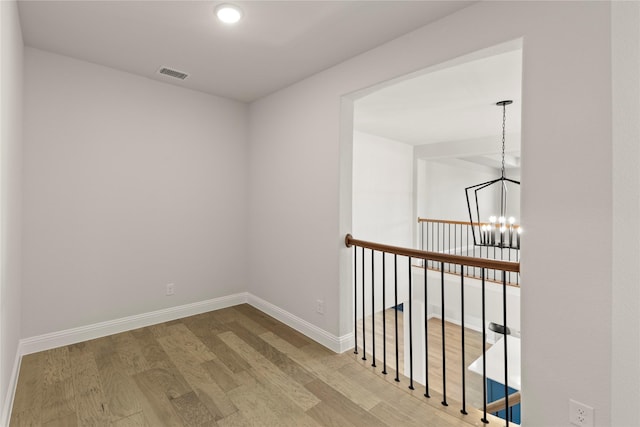 corridor with baseboards, visible vents, a chandelier, and wood finished floors