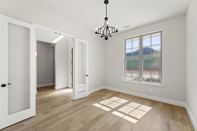 spare room featuring light wood finished floors, baseboards, visible vents, french doors, and a chandelier