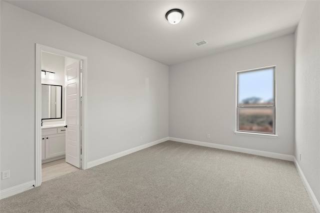 unfurnished bedroom with baseboards, ensuite bath, visible vents, and light colored carpet