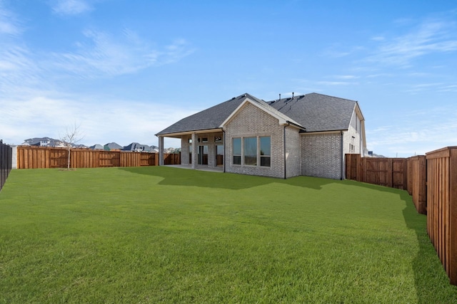 back of house featuring a shingled roof, brick siding, a yard, and a fenced backyard