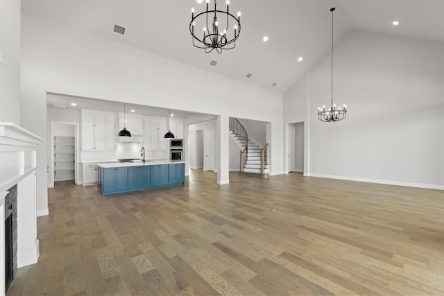 unfurnished living room featuring a fireplace, light wood finished floors, visible vents, stairway, and a chandelier