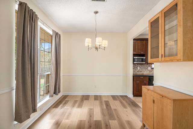 unfurnished dining area featuring an inviting chandelier, a textured ceiling, and light hardwood / wood-style floors