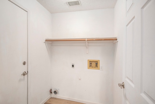 clothes washing area featuring light hardwood / wood-style flooring, electric dryer hookup, washer hookup, a textured ceiling, and hookup for a gas dryer