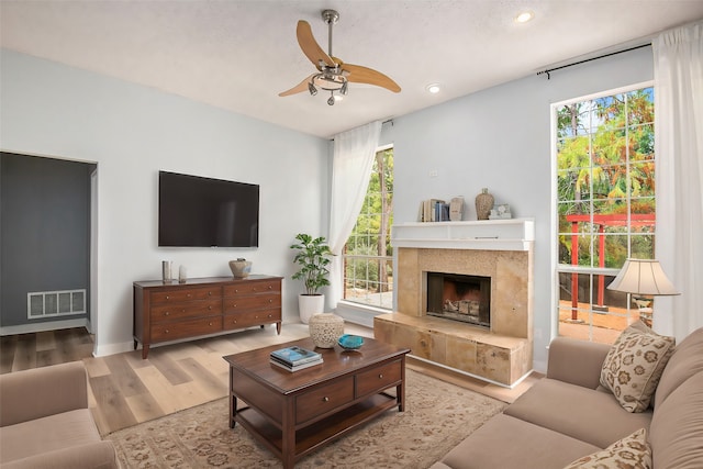 living room featuring ceiling fan, wood-type flooring, a high end fireplace, and a wealth of natural light