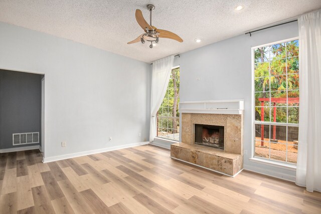 unfurnished living room with ceiling fan, a textured ceiling, a fireplace, and light hardwood / wood-style flooring