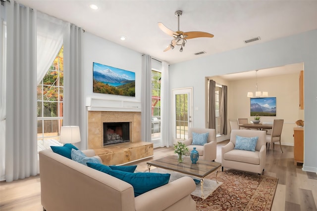 living room with a tile fireplace, ceiling fan, and light wood-type flooring