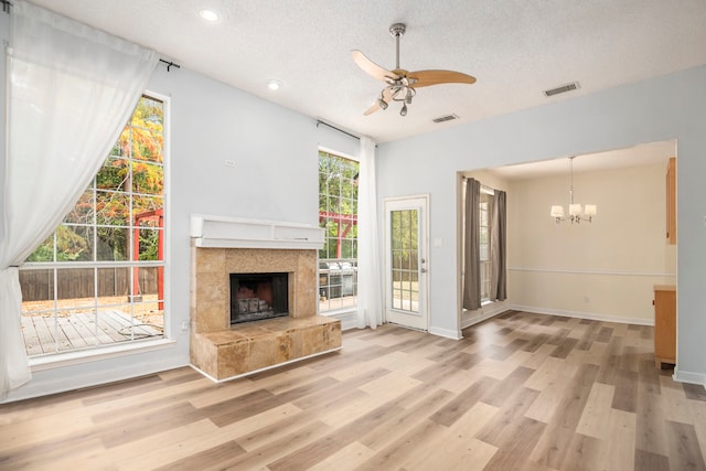 unfurnished living room featuring a tiled fireplace, ceiling fan with notable chandelier, a textured ceiling, and light wood-type flooring