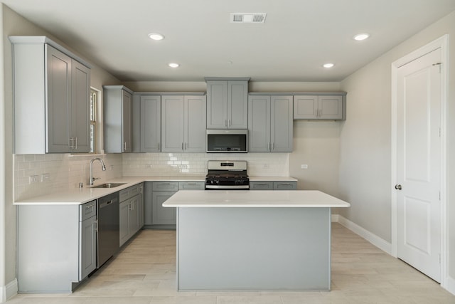 kitchen featuring appliances with stainless steel finishes, a center island, sink, and gray cabinetry