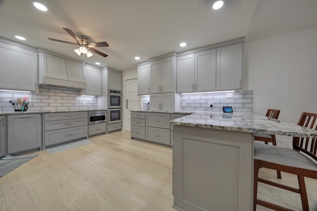 kitchen with kitchen peninsula, a breakfast bar, light wood-type flooring, gray cabinets, and tasteful backsplash