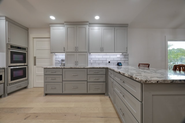 kitchen featuring double oven, light stone countertops, gray cabinetry, and backsplash