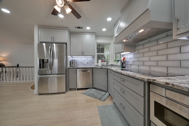 kitchen with gray cabinetry, tasteful backsplash, light stone countertops, appliances with stainless steel finishes, and custom exhaust hood