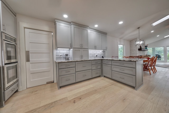 kitchen featuring decorative backsplash, kitchen peninsula, gray cabinetry, lofted ceiling with skylight, and light hardwood / wood-style floors