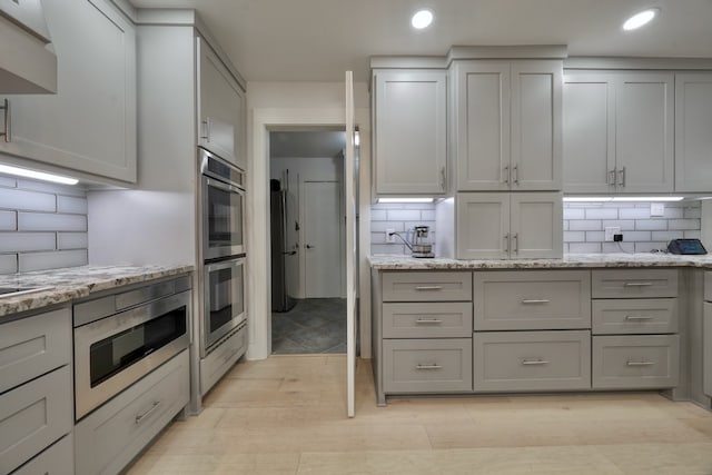 kitchen with gray cabinetry, tasteful backsplash, light stone countertops, and stainless steel appliances