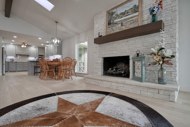 living room with ceiling fan with notable chandelier, vaulted ceiling with beams, a fireplace, and light hardwood / wood-style floors