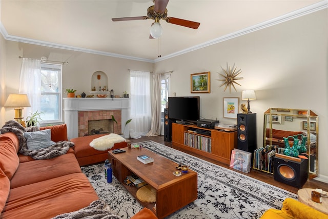 living room featuring ornamental molding, hardwood / wood-style floors, a tiled fireplace, and ceiling fan