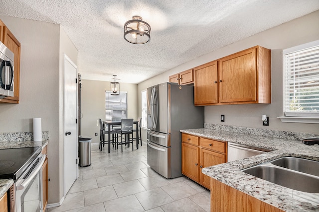 kitchen featuring hanging light fixtures, light stone counters, a textured ceiling, stainless steel appliances, and sink