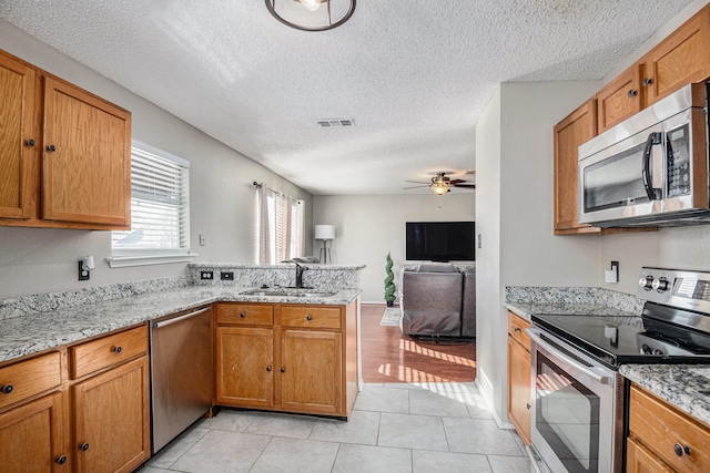 kitchen with kitchen peninsula, ceiling fan, appliances with stainless steel finishes, light tile patterned floors, and sink