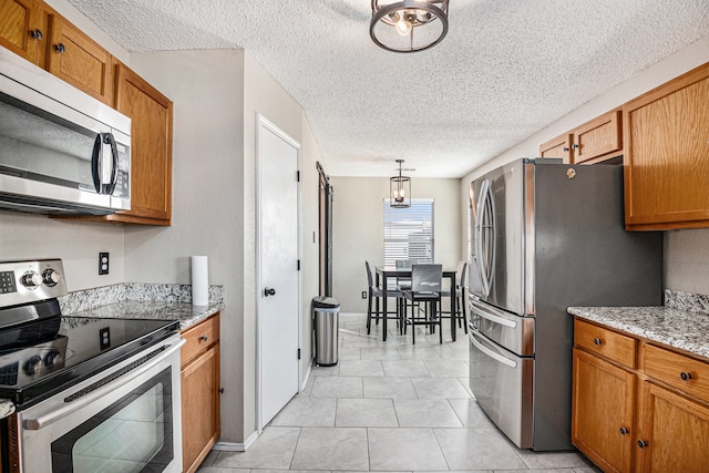 kitchen featuring appliances with stainless steel finishes, a textured ceiling, hanging light fixtures, light stone counters, and light tile patterned floors