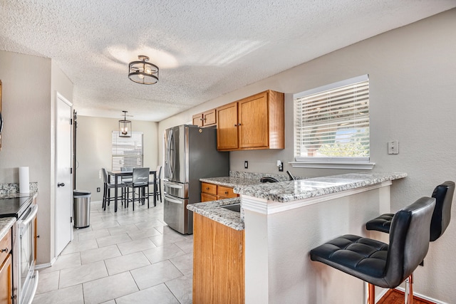 kitchen featuring a breakfast bar area, kitchen peninsula, stainless steel appliances, light stone counters, and a textured ceiling