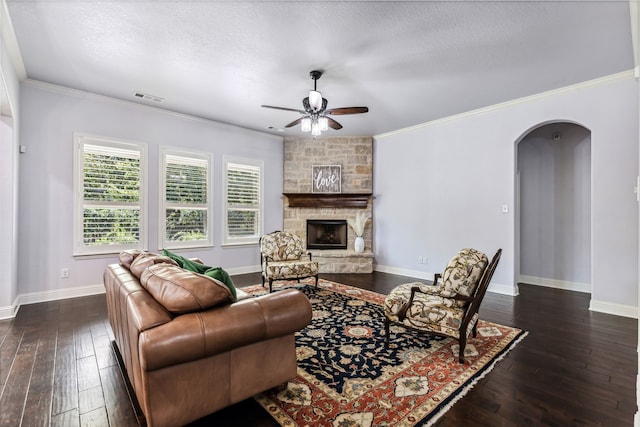 living room featuring ceiling fan, dark hardwood / wood-style flooring, a textured ceiling, a stone fireplace, and crown molding