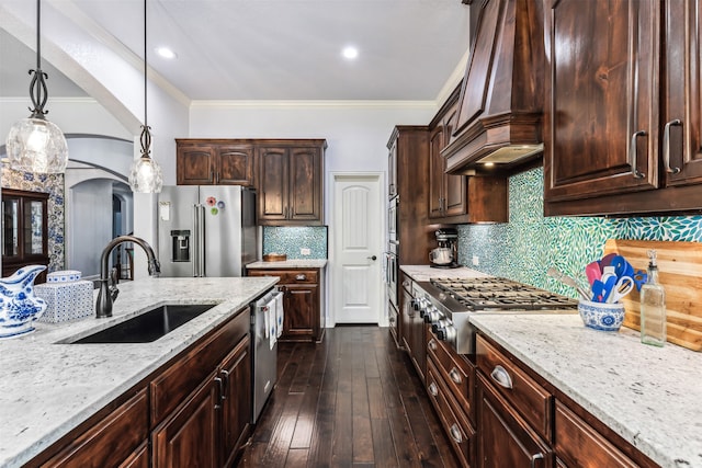 kitchen with appliances with stainless steel finishes, sink, dark brown cabinets, pendant lighting, and custom range hood