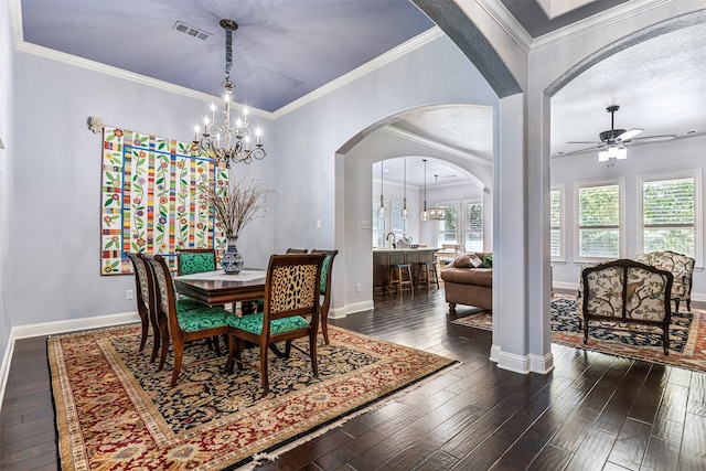 dining area with dark wood-type flooring, crown molding, and ceiling fan with notable chandelier