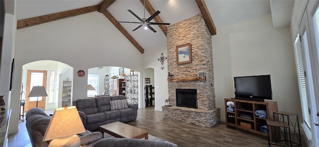 living room with a ceiling fan, dark wood-style floors, a stone fireplace, high vaulted ceiling, and beam ceiling