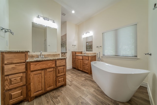 full bath with wood finished floors, a freestanding tub, a sink, and two vanities