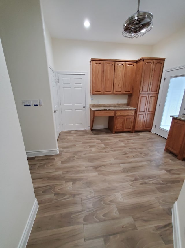 kitchen with baseboards, light wood-style floors, built in study area, and brown cabinets