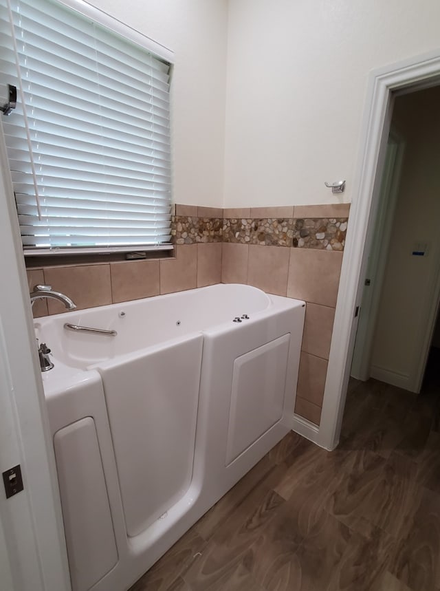 bathroom with a wainscoted wall, wood finished floors, a bath, and tile walls