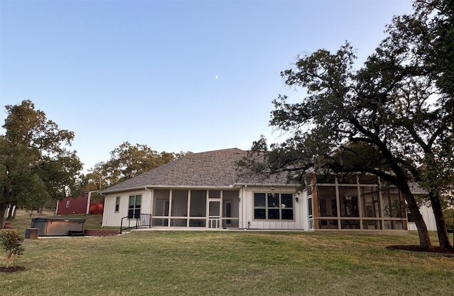 rear view of property with a sunroom, a hot tub, and a lawn