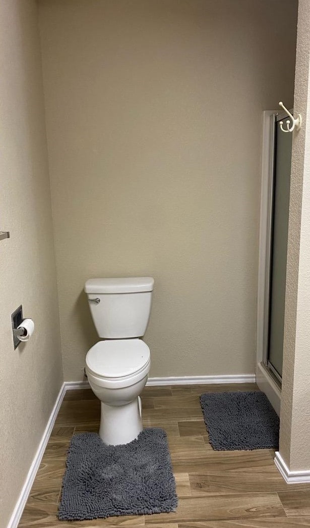 bathroom featuring a shower with door, toilet, and wood-type flooring