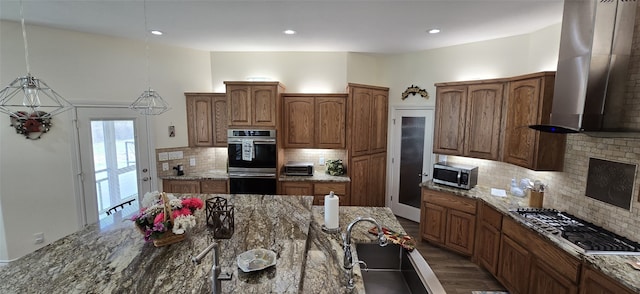 kitchen with extractor fan, stainless steel appliances, brown cabinets, dark stone counters, and pendant lighting