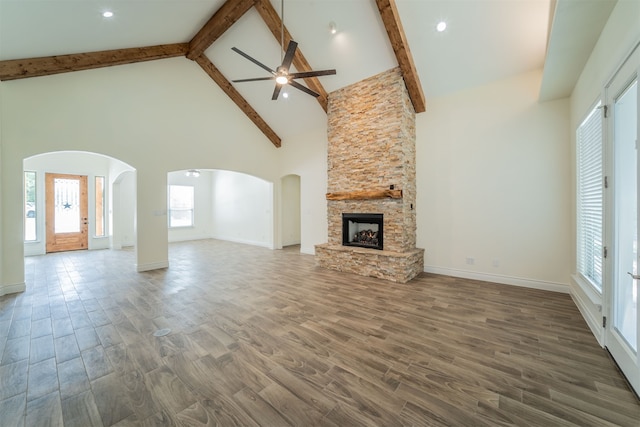 unfurnished living room with a stone fireplace, beamed ceiling, dark hardwood / wood-style flooring, high vaulted ceiling, and ceiling fan