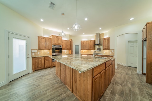 kitchen with a large island, wall chimney range hood, light hardwood / wood-style flooring, and hanging light fixtures