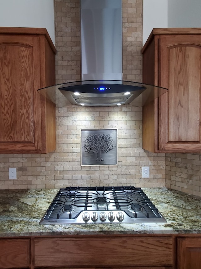 kitchen featuring light stone countertops, wall chimney exhaust hood, stainless steel gas stovetop, and tasteful backsplash