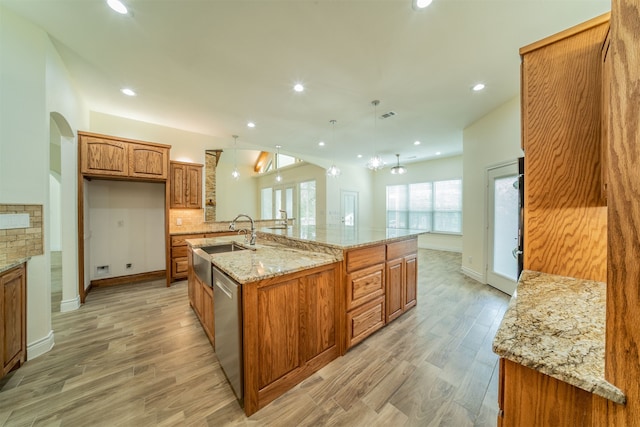 kitchen with dishwasher, a large island, light hardwood / wood-style floors, decorative light fixtures, and light stone counters