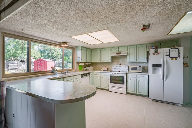 kitchen featuring sink, kitchen peninsula, green cabinets, white appliances, and decorative backsplash