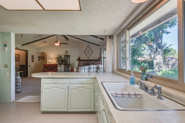 kitchen with sink, vaulted ceiling with beams, a textured ceiling, light tile patterned floors, and kitchen peninsula