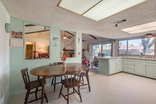 tiled dining room featuring ceiling fan, a brick fireplace, and a textured ceiling