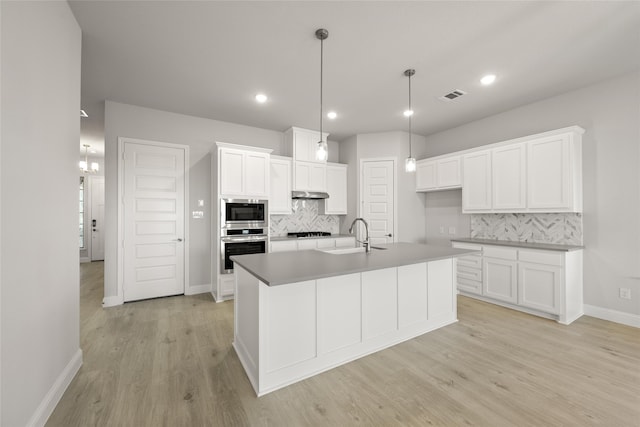 kitchen featuring light wood-type flooring, backsplash, sink, a center island with sink, and white cabinets