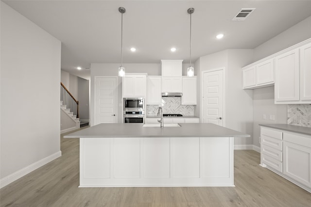 kitchen with light wood-type flooring, backsplash, stainless steel appliances, and a kitchen island with sink