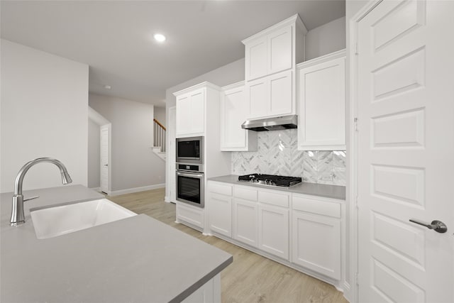 kitchen featuring appliances with stainless steel finishes, tasteful backsplash, white cabinetry, sink, and light hardwood / wood-style flooring