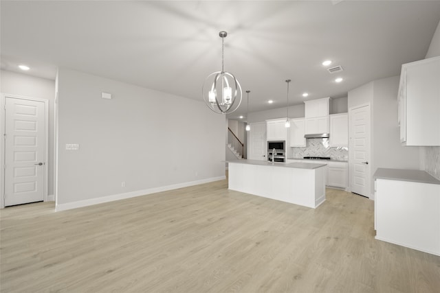 kitchen with a kitchen island with sink, hanging light fixtures, decorative backsplash, white cabinets, and light wood-type flooring