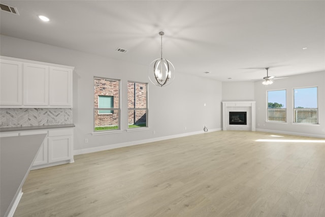 unfurnished living room with ceiling fan with notable chandelier and light wood-type flooring