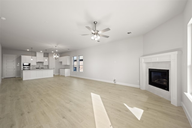 unfurnished living room featuring a tile fireplace, light hardwood / wood-style floors, and ceiling fan with notable chandelier