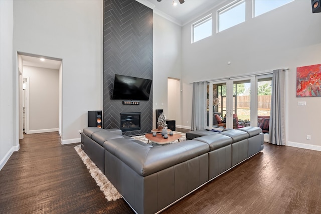 living room featuring a towering ceiling, crown molding, dark wood-type flooring, and a fireplace