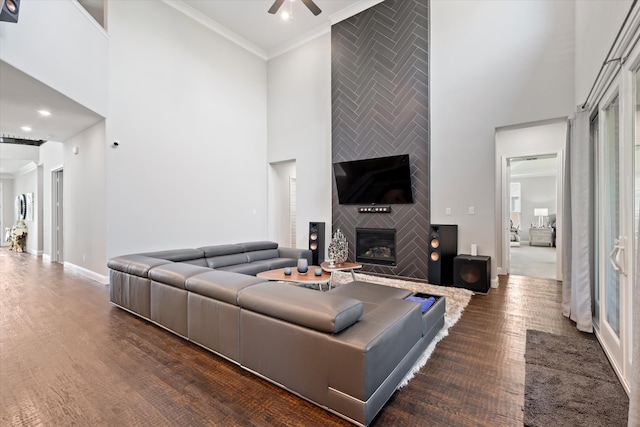 living room with crown molding, a towering ceiling, dark hardwood / wood-style flooring, and a fireplace