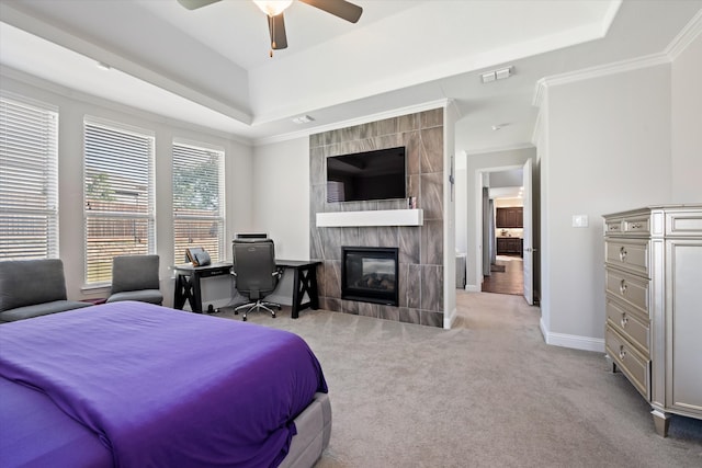 bedroom with a tray ceiling, a tiled fireplace, ceiling fan, light carpet, and ornamental molding