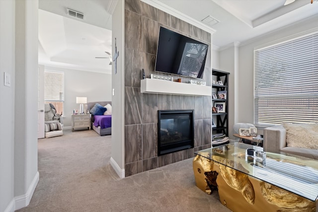 carpeted living room with crown molding, a tiled fireplace, a tray ceiling, and ceiling fan